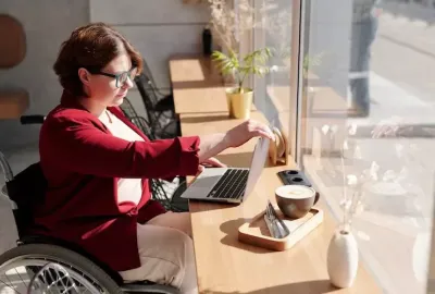 a woman in a wheelchair reading about living with cerebral palsy on a laptop