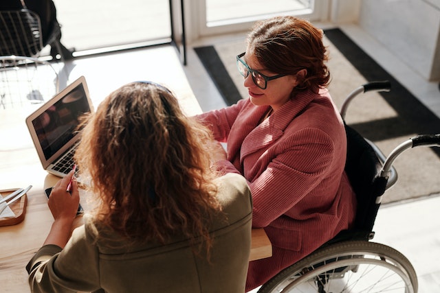 Two women sitting at a table and talking about strategies for wheelchair users to improve sleep