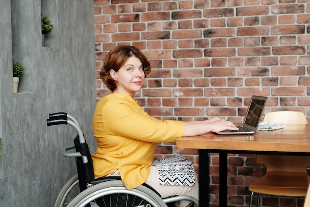 A person in a yellow sweater in a wheelchair using a laptop to research strategies for wheelchair users to improve sleep